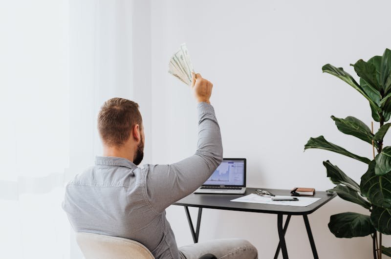 A man in a home office raises cash, symbolizing financial success and achievement.